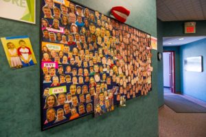 Bulletin board on a dark green wall with before and after photos attached to it.