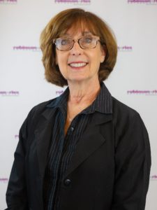 Denise, in a black and grey long sleeve shirt with a white background.